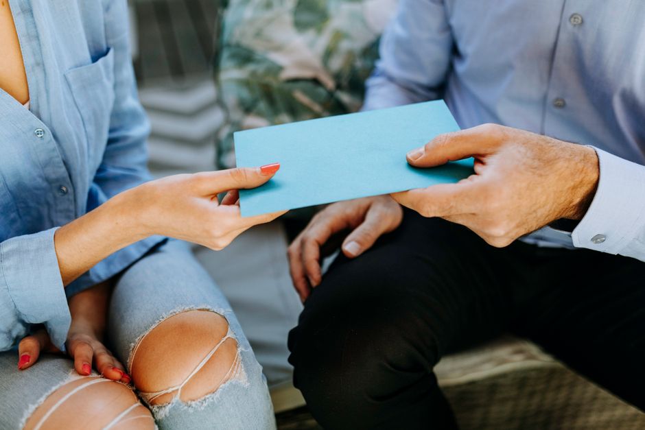 Close-up of two people exchanging a blue envelope, symbolizing communication or sharing.