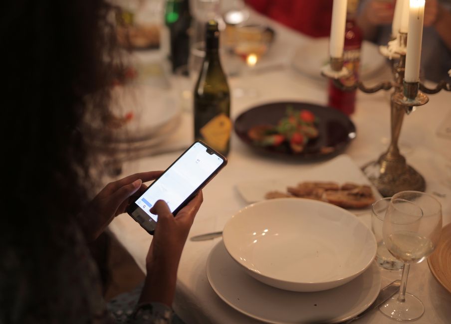 A cozy dinner setting with a woman using a smartphone at a candlelit table.